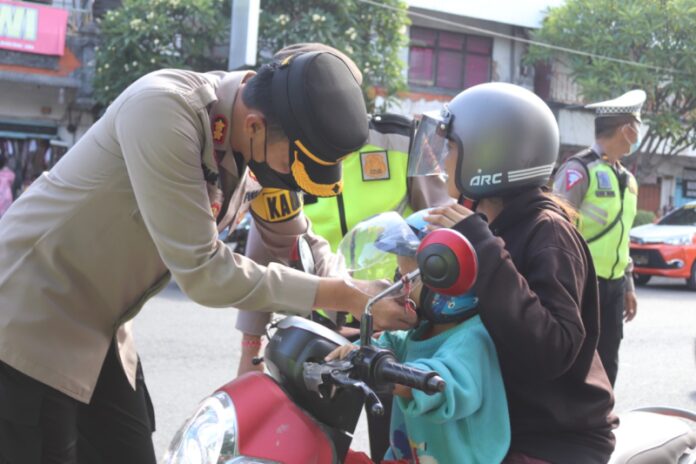 Kapolres Buleleng AKBP I Made Dhanuardana, S.I.K., M.H ketika memasang helm untuk anak dari salah satu pengendara yang melintas di Jalan Ponogoro, Singaraja